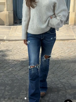 Bootcut jeans med slitningar och broderi - Snygga mörkblå bootcut jeans med slitna detaljer på knäna och låren. Jeansen har vit kontrastsöm och broderade fickor bak som ger en cool vibe. Modellen är lågmidjad och har klassisk femficksdesign. Perfekta för dig som gillar en avslappnad och trendig stil. Ej använda då de va en storlek för stora. Original priset är 399kr säljer för 300kr.💕