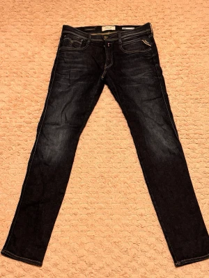 Replay Hyperflex Anbass mörkblå jeans - Snygga Replay Hyperflex Anbass jeans i mörkblå tvätt med klassisk femficksdesign och kontrastsömmar. Slim fit-modell med stretchigt material som sitter skönt och följer kroppen. Märkespatch i brunt läder baktill och diskret Replay-logga.