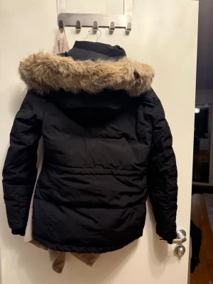 Canada Goose med päls i väldigt gott skick! - Säljer en svart dunjacka från Canada Goose med snygg päls på huvan och klassisk logga på ärmen. Jackan har dragkedja framtill, två fickor med dragkedja och quiltad design. Perfekt för kalla dagar med stil.