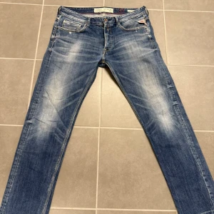 Replay Ronas blå jeans, storlek 33 - Snygga Replay Ronas jeans i klassisk blå tvätt med slitningar och kontrastsömmar. Modellen har fem fickor, knappgylf och Replay-logga på myntfickan. Jeansen är raka i benen och har en normal passform, tillverkade i mjukt jeanstyg för skön känsla.