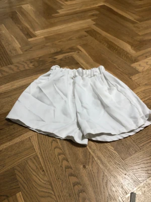Vita loose shorts med resårmidja - Säljer ett par vita shorts med loose fit och resår i midjan. De har en avslappnad passform och är perfekta för varma dagar. Materialet känns mjukt och svalt, troligen bomull eller polyester. Enkla att matcha med allt och superbekväma.