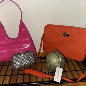 Fyra trendiga väskor i olika färger - Fyra snygga väskor: en rosa axelväska i glansigt syntet, en orange datorväska från Michael Kors i strukturmaterial, en glittrig silver clutch med pärlor och en rund grön glittrig kuvertväska med fransar från NLY Accessories. Perfekta för att sticka ut med färg och glitter.