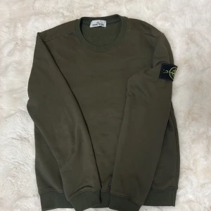 Grön Stone Island sweatshirt  - Säljer en snygg olivgrön sweatshirt från Stone Island i storlek S. Tröjan har det ikoniska Stone Island-märket på vänster ärm. Perfekt för dig som gillar streetwear och stilrena plagg. ‼️pris går att diskuteras‼️