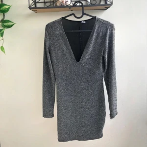 Glittrig silver kortklänning med v-ringning - Supersnygg silveraktig glittrig kortklänning med djup v-ringning och långa ärmar. Perfekt för nyår. Den är använd en gång o de va på nyår för några år sedan. Den är M men passar L, den har stretch i.