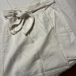 Vit jeans kortkjol med knyt från Rut&Circle - Snygg vit kortkjol från Rut&Circle i storlek S i jeans Kjolen har ett stilrent knytband i midjan och är gjord i mjuk bomull. Perfekt för dig som gillar minimalistisk och fräsch stil. Passformen är normal och kjolen har en enkel, klassisk design.