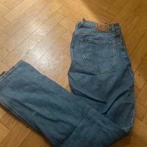 Blå jeans från Lee, modell WEST - Säljer ett par klassiska blå jeans från Lee, modell WEST. Jeansen har rak passform och normal midja, med Lee-logga på bakfickan och läderpatch i midjan. Materialet är slitstarkt denim i bomull. Perfekt för dig som gillar tidlös stil och bekväma jeans.