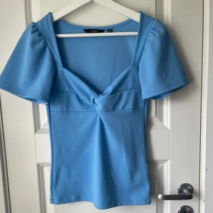 Ljusblå topp med knutdetalj - Säljer en ljusblå topp från Vero Moda med korta puffärmar och snygg knutdetalj framtill. Använd en gång🫶🏻