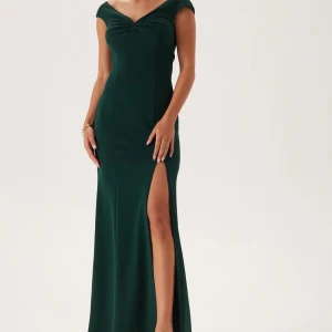 Mörkgrön långklänning med slits - Elegant mörkgrön långklänning med offshoulder och v-ringad omlottdesign. Klänningen har en hög slits på ena sidan och figurnära passform som framhäver siluetten. Perfekt för bal eller festliga tillfällen. Materialet är mjukt och följsamt, troligtvis polyester. Perfekt balklänning🩷(kan diskuteras pris)
