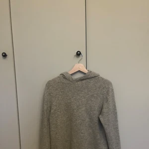 Grå kashmir hoodie med huva - Mysig grå hoodie i kashmir material med huva och långa ärmar. Perfekt för kyliga dagar och har en enkel, clean look utan detaljer eller mönster. Passformen är normal och färgen är neutral, vilket gör den lätt att matcha med andra plagg.