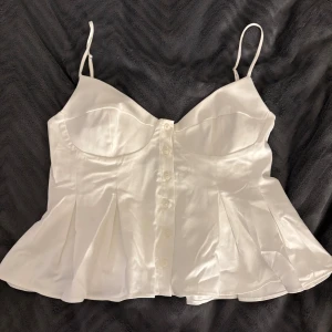 Vit korsett-topp från Zara i satin - Supersnygg vit korsett-topp från Zara. Toppen har smala axelband, knappar där fram och volang🤍