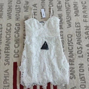 Vit spetsklänning från Gina Tricot - Supersöt vit kort klänning från Gina Tricot med 3D-blommig spets och tunna axelband. V-ringad upptill och detaljerad med blommönster över hela klänningen. Perfekt för sommarens alla tillfällen, riktigt fräsch och trendig look.