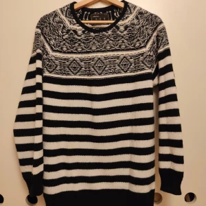 Svartvit stickad tröja med mönster - Snygg stickad tröja från Collezione i svart och vitt med breda ränder och grafiskt mönster upptill. Rund hals och långa ärmar med ribbade muddar. Perfekt för dig som gillar klassisk stil med en twist.