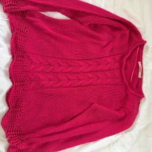 Rosa stickad tröja från Rosebud - Säljer en snygg rosa stickad tröja från Rosebud med långärmad design. Tröjan har ett unikt mönster med flätstickning och dekorativa hål längs nederkanten. Passar S-M