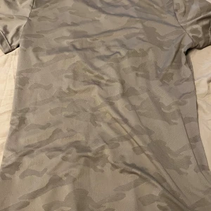 Camo t-shirt från Björn Borg - Snygg beige t-shirt från Björn Borg med diskret camouflage-mönster och vit mesh-remsa med logga på ryggen. Tillverkad i lätt polyester som andas, perfekt för träning. Kortärmad och med rund hals för en sportig vibe.