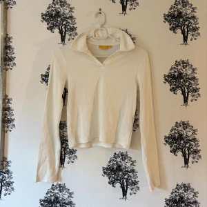 Vit ribbad pikétröja från Gina Tricot - Säljer en fräsch vit pikétröja från Gina Tricot med ribbad struktur och klassisk krage. Tröjan har lång ärm och en snygg v-ringad hals. Perfekt för dig som gillar stilrena och enkla plagg med lite edge.