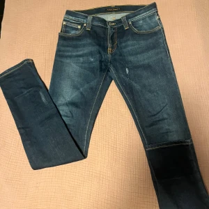 Mörkblå Nudie Jeans Skinny - Snygga mörkblå jeans från Nudie Jeans med klassisk gul söm och vågdetalj på bakfickorna. Modellen är skinny med låg midja och tillverkad i mjukt jeanstyg. Perfekt passform och cool faded effekt på benen. Ett litet hål som syns på bild 4 men går att sy 🪡 