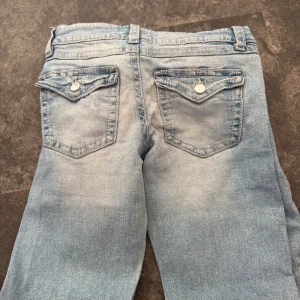 Ljusblå jeans från Gina Tricot - Snygga ljusblå jeans från Gina Tricot i storlek 158. Klassisk femficksmodell med två bakfickor som har lock och knappdetalj.