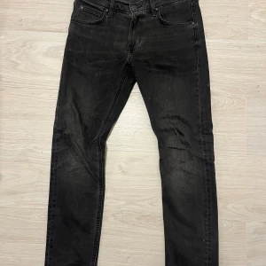 Svarta Lee jeans W29 L30 Slim Fit - Svarta jeans från Lee, modell Luke, med med slim fit passform och raka ben. Materialet är mjukt denim i bomull med lite stretch för skön passform. Perfekt för dig som gillar stilrena och tidlösa jeans.