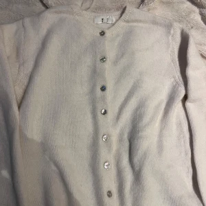 Vit kofta med glittriga knappar - Superfin vit kofta från Gina Tricot med glittriga knappar framtill. Koftan är stickad och har lång ärm, perfekt att slänga över en topp eller klänning. Enkel och stilren design som passar till allt.