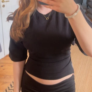 Svart croppad topp med kort ärm - Säljer en svart croppad topp med rund hals och korta ärmar. Toppen har en tight passform och är tillverkad i ett mjukt material som sitter snyggt mot kroppen. Perfekt att styla med jeans eller kjol för en cool look.