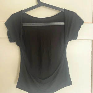 Svart topp med öppen rygg - Snygg svart topp med korta ärmar och en djup, öppen rygg som ger en cool vibe. Tunn och mjuk i materialet. 