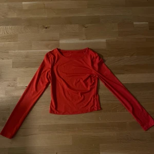 Röd långärmad topp med rund hals - Säljer en enkel och snygg röd långärmad topp med rundad halsringning. Modellen är croppad och har en slim passform som sitter snyggt på kroppen. Perfekt att styla med jeans eller kjol för en cool look. Materialet känns mjukt och stretchigt.