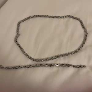 Silver kedjehalsband och armband - Snyggt set med halsband och armband i silverfärgad metall. Kedjorna har en robust, rektangulär länkdesign som ger en cool och modern vibe. Halsbandet är 56 cm långt och armbandet är 21 cm, båda med smidig karbinhake. Perfekt för dig som gillar chunky smycken.