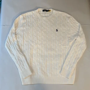 Vit kabelstickad tröja Polo Ralph Lauren - Vit kabelstickad tröja från Polo Ralph Lauren med klassisk rund hals och broderad marinblå logga på bröstet. Storlek M men passar även som L.
