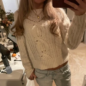 Vit stickadtröja - Säljer en vit stickad tröja med snyggt flätmönster framtill. Tröjan är croppad med bred ribbad kant nedtill och har långärmade ärmar. Perfekt för dig som gillar en chill och trendig look till jeans eller kjol.