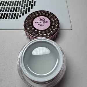 NG Starline Base Gel & White Gel - Två burkar nagelgel från NG Starline, en Base Gel och en Thick White Gel, båda på 30 ml. Burkarna är rosa med glittriga stenar och har en lyxig look. Gelen är transparent respektive vit och passar perfekt för nagelförlängning eller nail art.