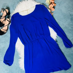 Kornblå kortklänning med lång ärm - Supersnygg kornblå klänning med lång ärm och elastisk midja som ger en schysst siluett. Klänningen har en rundad halsringning fram och en djup v-ringad rygg, vilket ger en cool kontrast. Materialet är mjukt och lätt, perfekt för att sticka ut med färg.