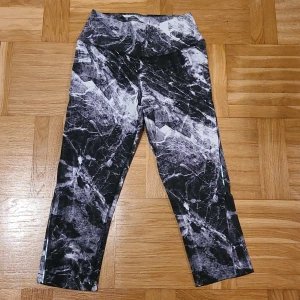Nike Dri-Fit leggings XS svart/vit - Nike Dri-Fit leggings i storlek XS med svart och vit marmorerat mönster. 3/4 längd på benen. Högmidjade och tillverkade i ett stretchigt syntetmaterial som andas, perfekta för träning. Snygg och modern look med croppad längd.