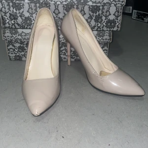 Beige pumps med spetsig tå och klack - Snygga beige pumps med spetsig tå och hög klack. Skorna har en stilren design i glansigt syntetmaterial och klassisk siluett. Perfekta för dig som vill ha en elegant look med en touch av nude-ton. Röd sula för extra statement. Skorna har ett inlägg vid tårna för en mer comfortabel användning. Pris kan diskuteras
