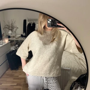 Beige stickad tröja med kort ärm - Mysig beige stickad tröja med korta, lite bredare ärmar och rund halsringning. Tröjan har en loose passform och är perfekt för dig som gillar en enkel och chill stil. Materialet är mjukt och ger en skön känsla mot huden. Passar till jeans eller mjukisbyxor.