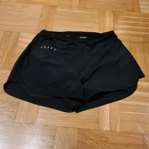 Svarta träningsshorts från Craft - Säljer ett par svarta träningsshorts från Craft i storlek S. De har ventilerande meshpaneler på sidorna och elastisk midja med diskret logga. Perfekta för löpning eller gym, riktigt sköna och lätta med sportig look.