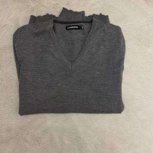 Grå v-ringad tröja från J.Lindeberg - Snygg grå v-ringad tröja från J.Lindeberg med diskret broderad logga på bröstet. Tröjan är stickad i mjukt material.Ny pris på tröjan är ungefär 1300!Perfekt för dig som gillar stilrena och klassiska plagg.