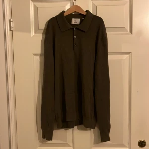 Brun stickad pikétröja från Bläck - Snygg brun stickad pikétröja från Bläck med klassisk krage och tre knappar framtill. Tröjan har långärmad design och är gjord i mjukt stickat material som känns chill och stilrent. Perfekt för dig som gillar enkel och clean look.