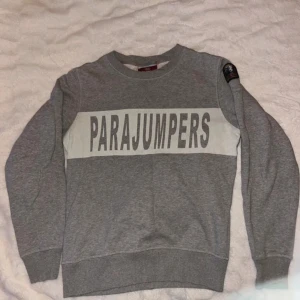Grå sweatshirt från Parajumpers - Snygg grå sweatshirt från Parajumpers med stort logotryck över bröstet och patch på ena ärmen. Tröjan har rund halsringning, ribbade muddar och är tillverkad i mjuk bomullsblandning. Perfekt för en chill och stilren look.