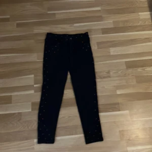 Svarta skinny byxor med mönster storlek 153-162 - Svarta byxor med skinny passform och hög midja. Byxorna har små orange och blå trianglar som mönster på fickor, midja och längs benen. De har klassisk knapp och dragkedja framtill samt fickor både fram och bak. Materialet känns mjukt och stretchigt.