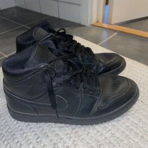 Jordan 1 Mid black  - Säljer ett par helsvarta Nike Air Jordan 1 Mid med klassisk siluett och snörning. Skorna är tillverkade i skinn och har en rund tå samt platt sula. Perfekta för dig som gillar en clean och tidlös look. Skater stil!🏆nypris: 1300