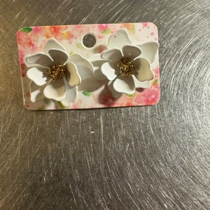 Vita blomformade örhängen - Superfina örhängen i form av vita blommor med guldfärgade detaljer i mitten. De har en tredimensionell design som verkligen sticker ut och ger en söt och unik look. Perfekta för dig som gillar blommiga accessoarer och vill ha något som syns.