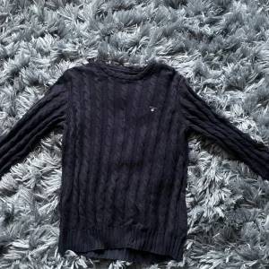 Mörkblå stickad tröja från GANT - Säljer en snygg mörkblå stickad tröja från GANT. Tröjan har ett klassiskt flätmönster och rund halsringning. Perfekt för kyligare dagar och ger en stilren look. Passar ungdomar i åldern 13-14 år.