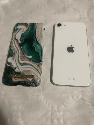 iPhone SE ( 2020) 64 GB  - iPhone SE ( 2020) 64 GB, fungerar utmärkt och iOS 26. Bank id och alla sådan appar fungerar. Inga sprickor ( bruksskick så repor förekommer men inget allvarligt ) se bilder. Fin telefon annars och fullt fungerande. Ett skal ingår 