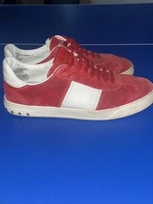 Valentino Rockrunner röda sneakers - Säljer ett par Valentino Rockrunner sneakers i rött mocka och vitt skinn. Skorna har klassiska nitar på hälen, röda skosnören och vit sula. Snygg kontrast mellan det röda och vita, samt ikonisk Valentino-logga på plösen. Perfekta för dig som vill sticka ut.