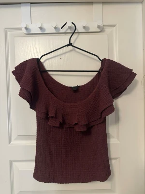Volangblus  - Säljer en vinröd blus i nyskick från Lindex i storlek S. Toppen har en strukturerad, stretchig yta och bred volang runt ringningen och axlarna. Jättesnygg att ha på fest eller till sommaren!💋😽 Priset kan förhandlas!