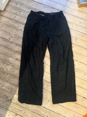 Svarta linnebyxor från Weekday - Säljer ett par svarta linnebyxor från Weekday med avslappnad passform och dragsko i midjan. Byxorna har raka ben och elastisk midja för extra komfort. Perfekta för en chill och stilren look.