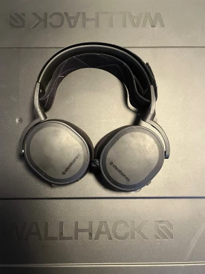 SteelSeries Arctis 7 wireless  - SteelSeries Arctis 7 trådlöst spelheadset med tillhörande USB-sändare och kabel. Over-ear design för hög komfort, justerbart huvudband. Viss kosmetisk slitage syns på kåporna men i gott skick. Perfekt för gaming med klart ljud och mikrofon.