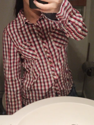 Rutig skjorta i rött och vitt - Säljer en rutig skjorta i rött, vitt och blått. Den är för stor på längden men för tight på armarna (köp inte om ni tränar armar). Den är lite stor i midjan men blir superfin om ni syr in den tight. Jag bär S/M och den sitter som en S. Jag är 155cm. 