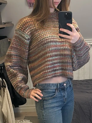 Randig croppad stickad tröja C.W. - Croppad stickad tröja från C.W. i storlek S. Tröjan har ett randigt mönster i bruna, orange, blå och beige toner. Den har lång ärm, ribbade muddar och en relaxed, loose fit. Perfekt för dig som gillar mysiga höstlooks! En av de skönaste tröjorna jag någonsin haft på mig, hur mjuk som helst!