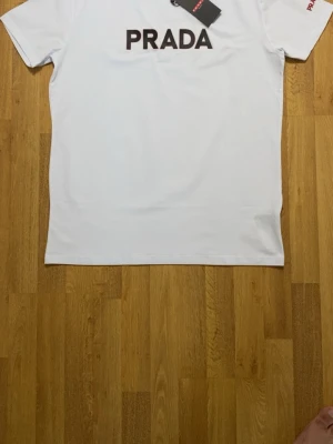 Vit  t-shirt med logga - Snygg vit t-shirt i mjuk bomull. Stor svart logga framtill med röd kant och liten röd detalj vid nederkanten. Klassisk rund halsringning och korta ärmar. Perfekt för dig som gillar stilrena designer och exklusiva märken.